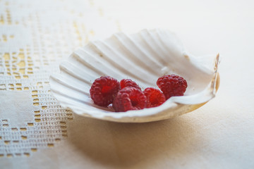 a handful of raspberries lies in a mother of pearl plate in the form of a shell on the table with a...