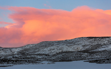 Snowy hill landscape at sunset with pink clouds and blue sky