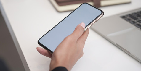 Cropped shot view of woman hands holding smart phone with blank copy space screen for your text message or information content, female reading text message on cell telephone during in urban setting. 