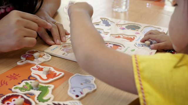 Cute little child girl having fun playing with montessori wood material for the animal learning at class room. Concept of educational toys for young children.
