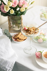 Breakfast concept, Sunday brunch in a restaurant. Light granola with Greek yogurt in a glass goblet, coffee, light sweets and flowers on a snow-white tablecloth.