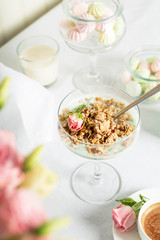 Breakfast at the restaurant. Light granola with Greek yogurt in a glass goblet, perfectly preserved on a white tablecloth amid flowers and sweets.
