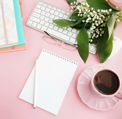 Pink flat lay top view women's office desk . Female workspace with laptop, white spring flowers lilies, accessories, notebooks mock up, glasses, cup of coffee on pale pink background. Copy space