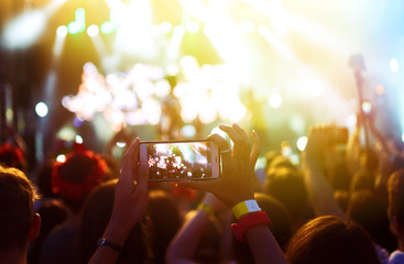 Hand with a phone records live music festival. People taking photographs with smart phone during a...