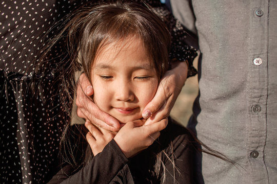 Portrait Of Little Asian Girl Being Hugged By Her Parents Outdoors