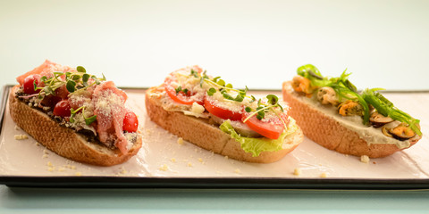 Three traditional Italian bruschetta with parmesan cheese, tomato, prosciutto meat, mushrooms, seasoned with herbs