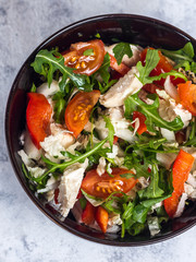 Salad with chicken, tomato and spinach in a dark bowl on a light background