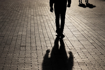 Silhouette and shadow of a man walking walking towards a couple on a street. Concept of crime or robbery, relationships, jealousy, social issues