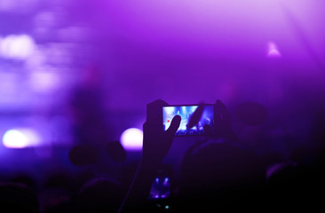 Hand with a phone records live music festival. People taking photographs with smart phone during a...
