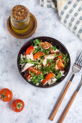 Salad with chicken, tomatoes and spinach with Beijing cabbage in a dark bowl with a napkin, butter and devices on a light background