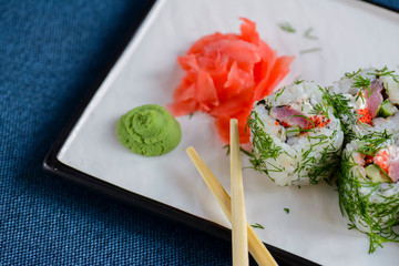 Salmon sushi rolls served on a white plate with ginger and wasabi sauce in a restaurant on table. Japanese cuisine.