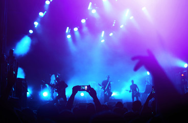 Hand with a phone records live music festival. People taking photographs with smart phone during a...