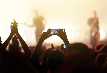 Hand with a phone records live music festival. People taking photographs with smart phone during a...