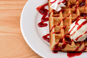 Plate of belgian waffles with ice cream and fruit strawberry caramel sauce on wooden table background