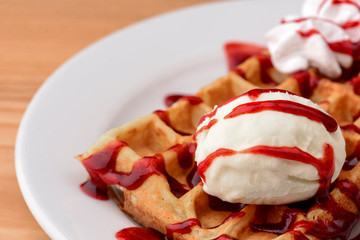 Plate of belgian waffles with ice cream and fruit strawberry caramel sauce on wooden table background