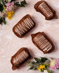 Chocolate pop cake with pink and yellow spring flowers on a marble background. Image with a top view. 