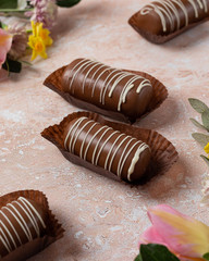 Chocolate pop cake with pink and yellow spring flowers on a marble background.