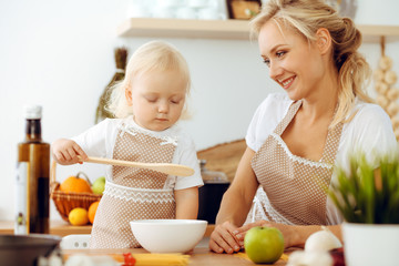 Happy mother and little daughter cooking in kitchen. Spending time all together, family fun concept