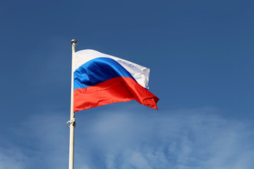 Naklejka na ściany i meble Russian flag waving on background of blue sky with clouds. Symbol of Russia, russian government and authority concept