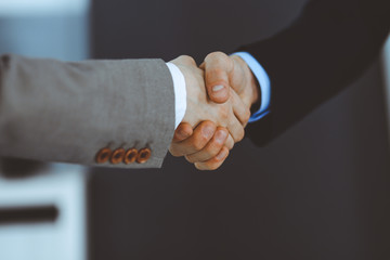 Obraz premium Business people shaking hands while standing with colleagues after meeting or negotiation, close-up. Group of unknown businessmen and women in modern office. Teamwork, partnership and handshake