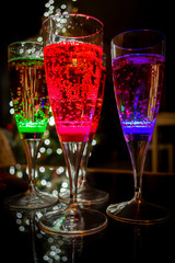 Colorful party glasses, red, blue and green, filled with champagne, cava or prosecco, on a dark and black background. Ready for bubbles and celebration. 