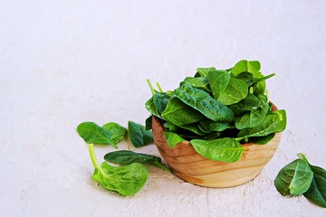 Fresh organic spinach in a wooden bowl on a light concrete background. Fresh greens. Copyspace.