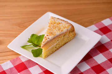 Slice of victoria sponge cake with cream filling, served with a mint leaf on a white plate on light wooden table