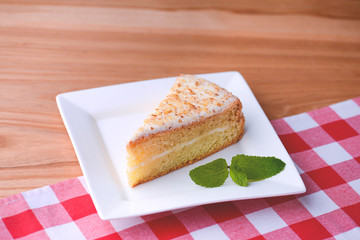 Slice of victoria sponge cake with cream filling, served with a mint leaf on a white plate on light wooden table