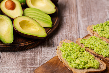 Avocado sandwiches next to cutted ones on wooden board