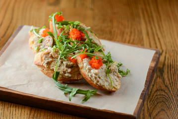 Italian bruschetta with salmon butter, capelin caviar, cherry tomatoes and parsley served on wooden cutting board