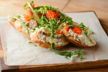 Italian bruschetta with salmon butter, capelin caviar, cherry tomatoes and parsley served on wooden cutting board