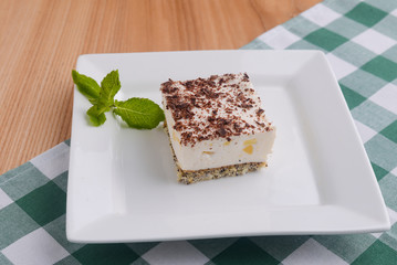Traditional Italian dessert tiramisu served on a white plate with a mint leaf in a restaurant. Italian cuisine, dessert.