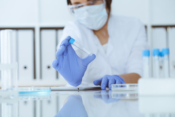 Close-up of professional female scientist in protective eyeglasses making experiment with reagents...