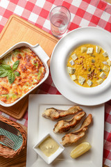 Traditional Italian cuisine, lasagna made with minced beef, pumpkin soup with seeds and cheese and fried fish. Top view.