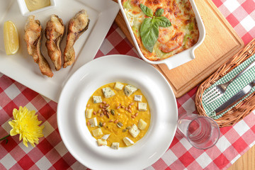 Traditional Italian cuisine, lasagna made with minced beef, pumpkin soup with seeds and cheese and fried fish. Top view.