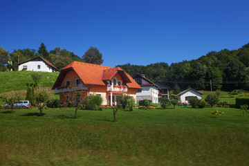 Fototapeta na wymiar Orange house Europe countryside among lush green summer landscape and blue sky