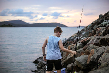 Fototapeta na wymiar Young boy fishing off rocks at twilight