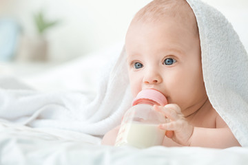 Portrait of cute little baby drinking milk from bottle on bed