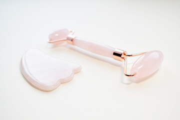 Pink Guasha massage tool on white background. Rose quartz jade roller. Skin care at home, anti-aging and lifting therapy. Top view. Copy space.