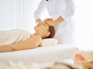 Beautiful woman enjoying facial massage with closed eyes in spa center. Relaxing treatment concept in medicine