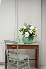 bouquet with white gerbera flowers in a green vase with a table and a chair a 