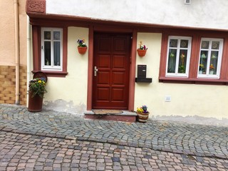 Old crooked tiny house with a wooden door and narrow windows on a paved street (Bacharach, Germany,...