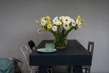 bouquet with gerberas in shades of white and yellow in a simple grey interior with a table and chairs