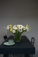 bouquet with gerberas in shades of white and yellow in a simple grey interior with a table and chairs