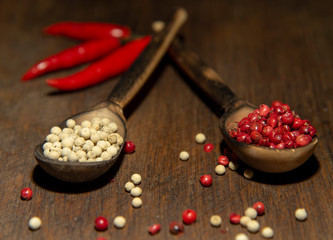 Two wooden spoons with red and white pepper on a wooden surface.