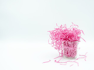 Side view of shredded pink paper overflowing a glass bin isolated on white background with copy space. Selective focus image