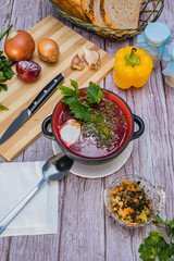 Red borsch, a national dish of Ukrainian cuisine. In the photo, borsch is a black ceramic with sour cream, green onions and garlic on a wooden background.