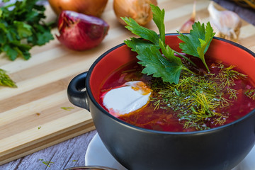 Red borsch, a national dish of Ukrainian cuisine. In the photo, borsch is a black ceramic with sour cream, green onions and garlic on a wooden background.