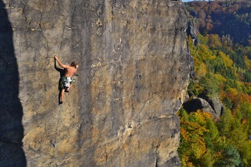 Young man is climbing on the sandstone rock in Sachsen Switzerland. Beautiful autumn day in Germany. - obrazy, fototapety, plakaty