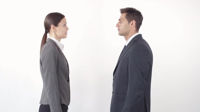 Medium shot of young businessman and businesswoman standing in front of each other on white background, talking and shaking hands